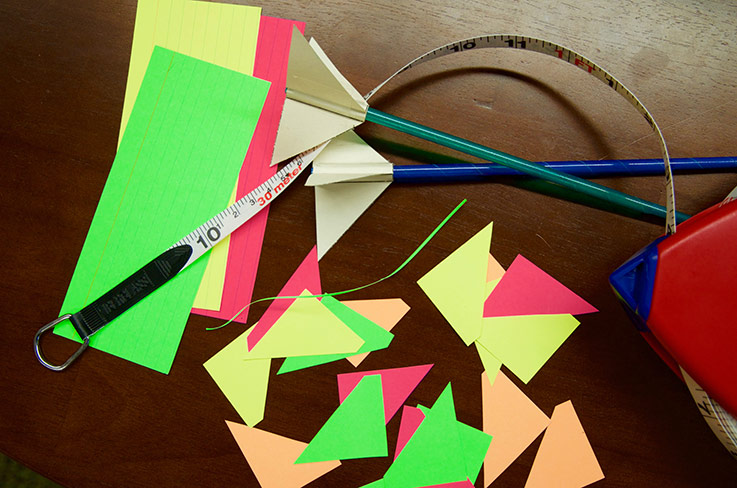 Two straw rockets on a table with more fins to add to the rockets and a tape measure for seeing how far the rockets fly.